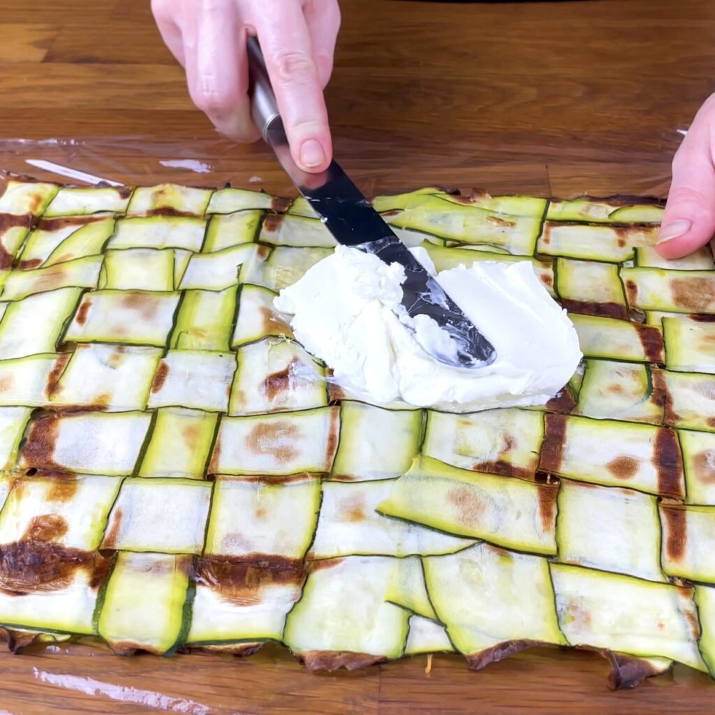 Spreading cream cheese on baked courgette base.