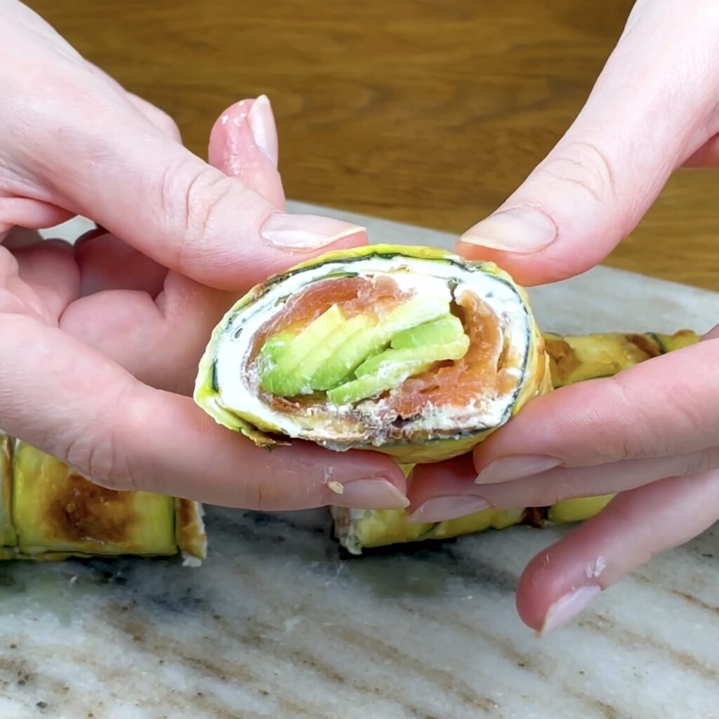 Slice of courgette salmon roll with layers of salmon, cream cheese, and avocado.