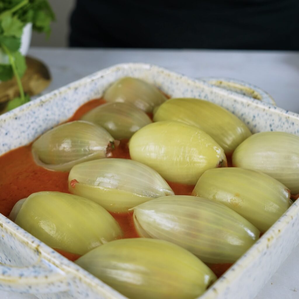 Stuffed onions arranged in a baking dish with tomato sauce at the bottom.