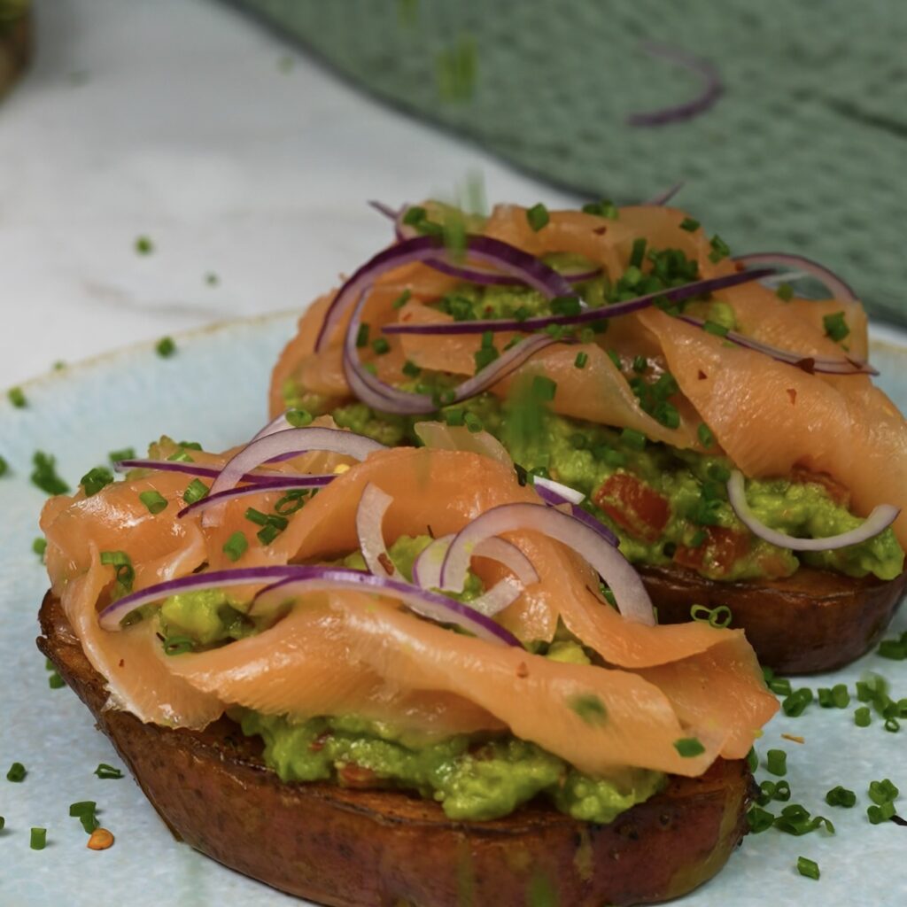 Sprinkling freshly chopped chives over potato toast topped with avocado and smoked salmon.