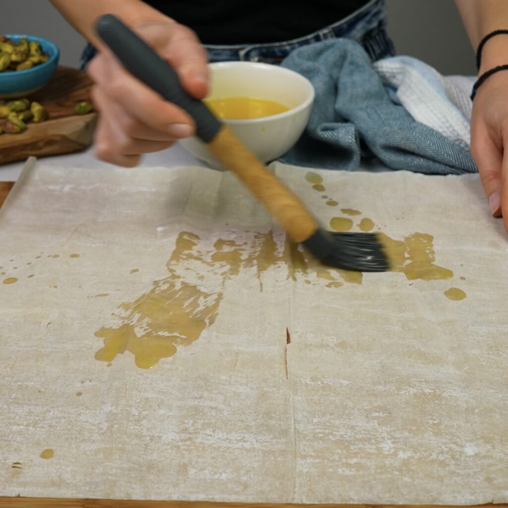 Brushing melted butter onto a sheet of filo pastry.