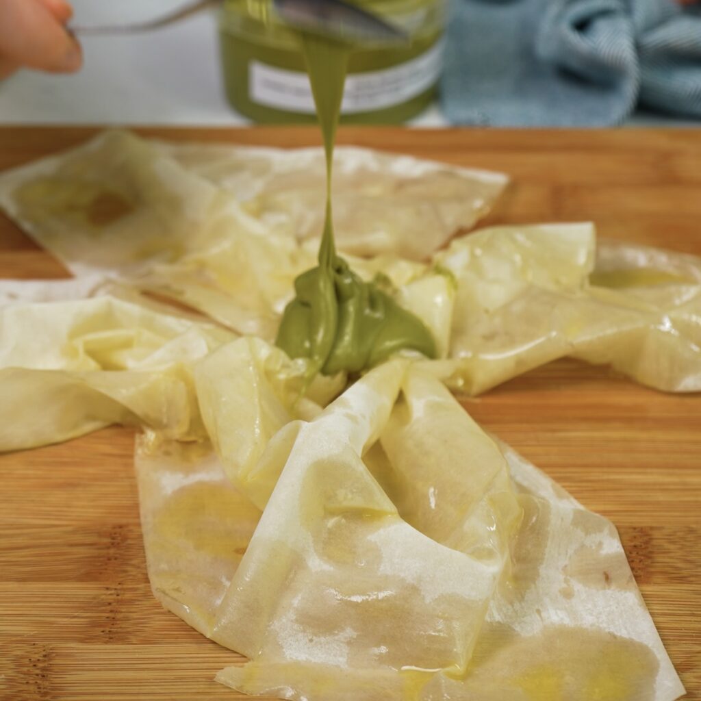 Adding pistachio paste to the centre of a folded filo sheet.