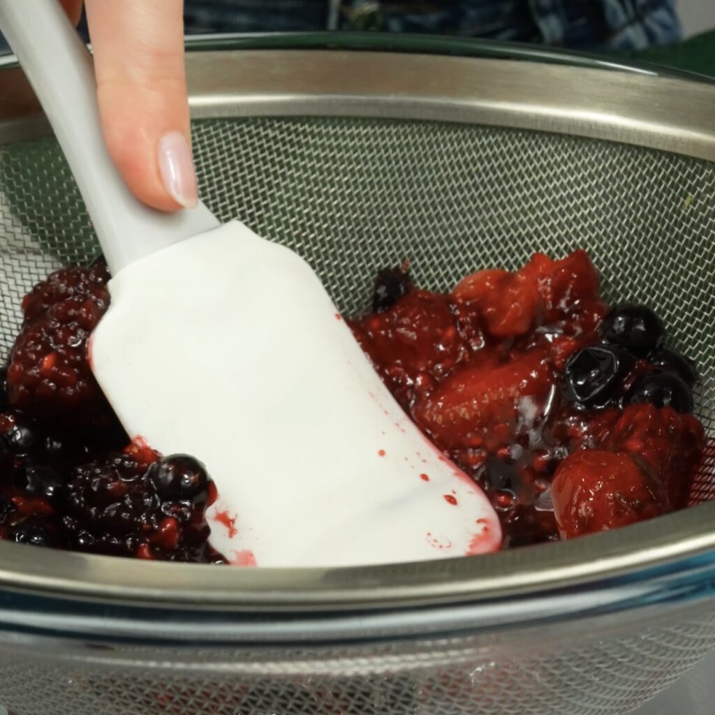 Straining berry purée through a sieve to remove seeds.