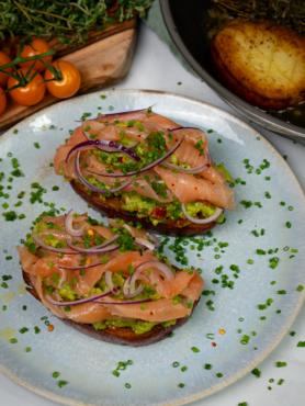 Potato toast topped with smashed avocado, smoked salmon, red onion slices, and fresh chives