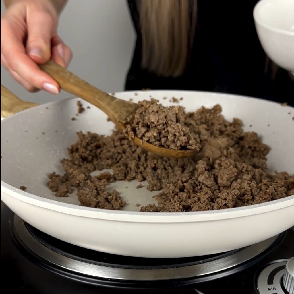 Minced beef browning in a skillet with golden edges forming.