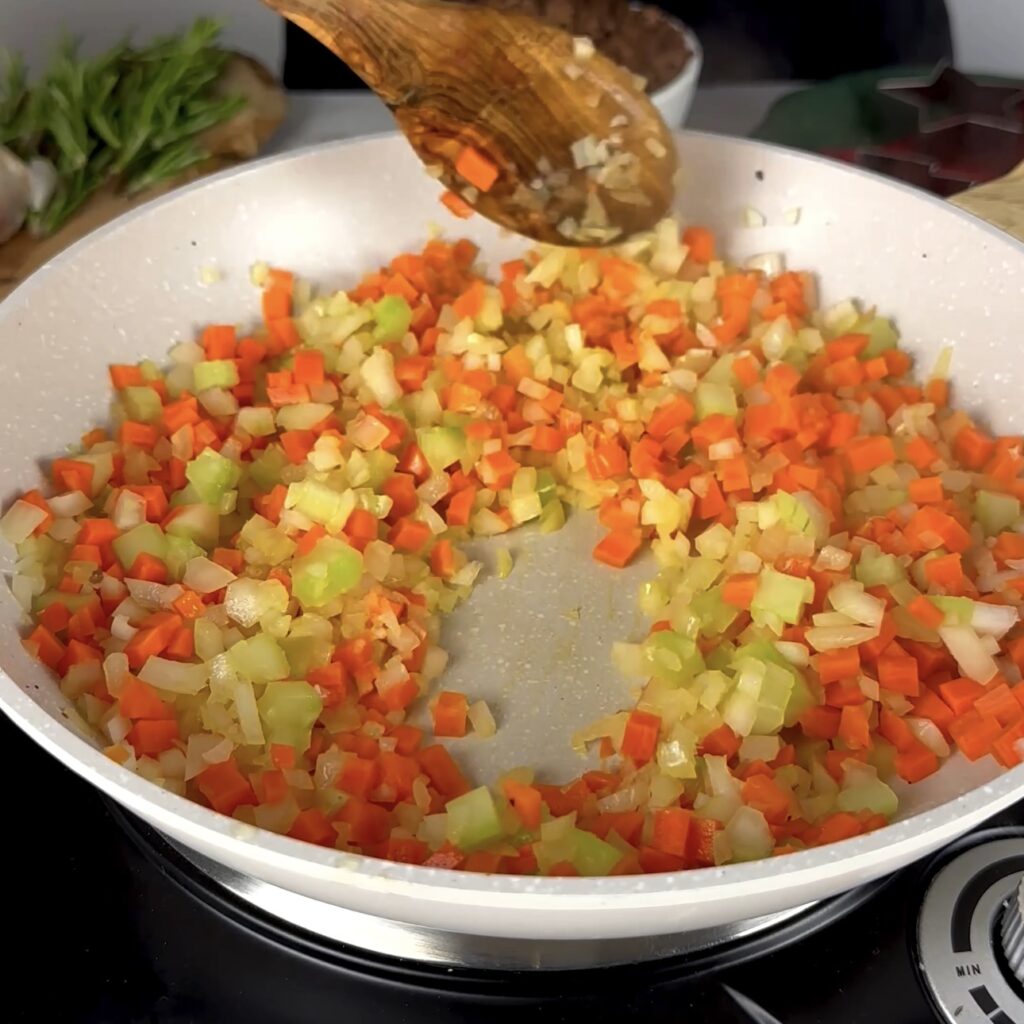 Onions, carrots, and celery sautéing in a skillet.