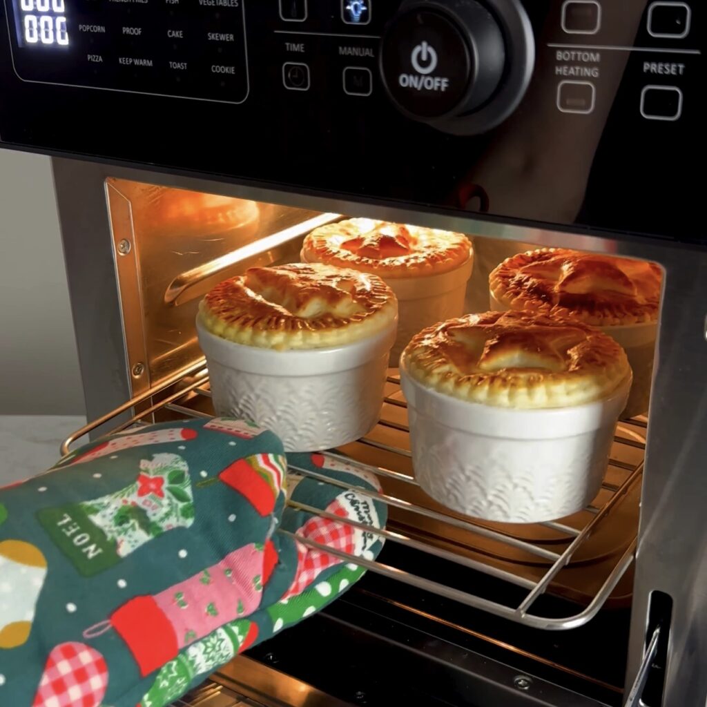 Individual Christmas pies baking in an air fryer with golden puff pastry tops.