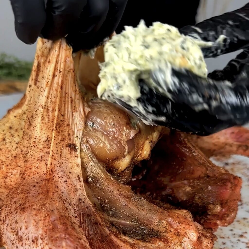 Spreading garlic herb butter under the skin of the chicken.