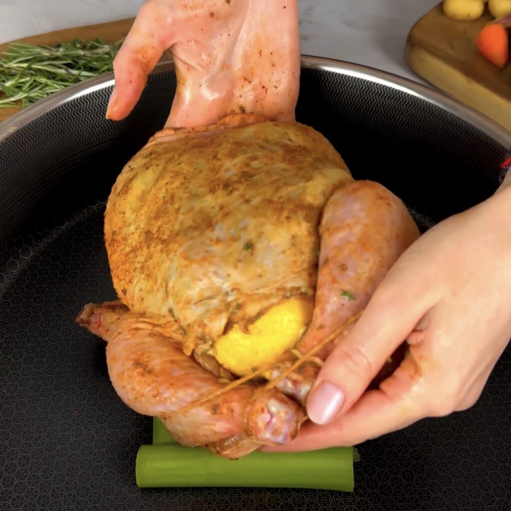 Placing the chicken on top of celery sticks in a roasting pan.