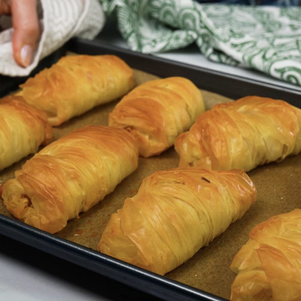 Golden, baked filo pastry buns on a tray.