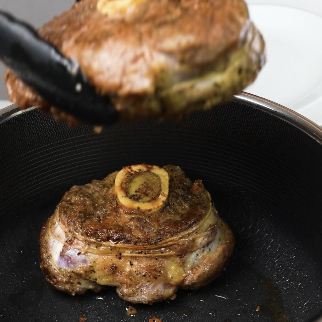 Searing beef shanks in a hot pan to develop a rich, golden crust.