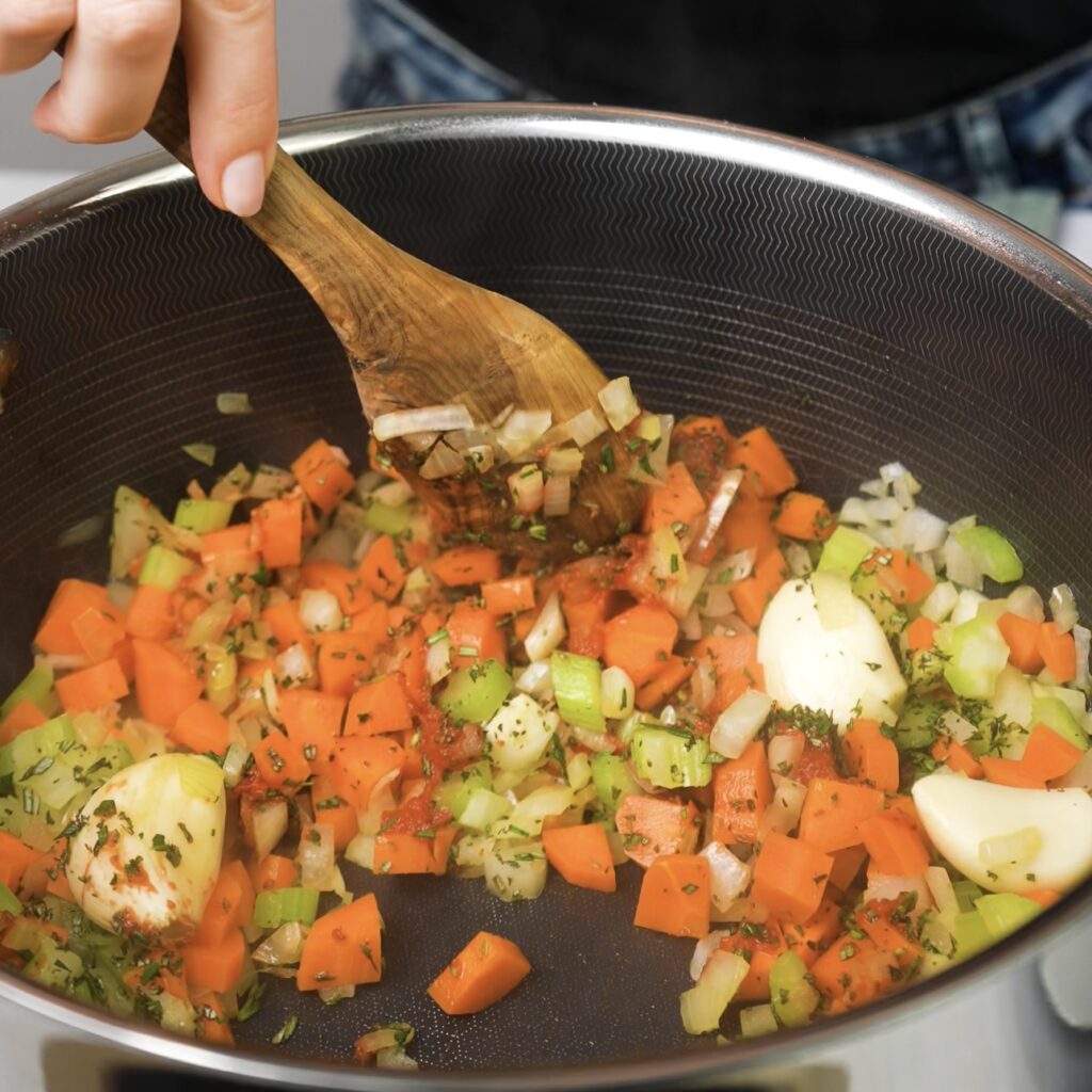 Cooking diced onion, carrots, celery, garlic, tomato paste, and herbs in a pot for braised beef shanks.