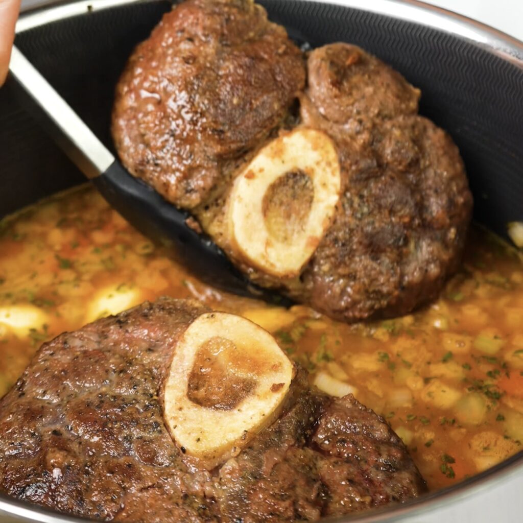 Returning beef shanks to the pot with sautéed vegetables and braising liquid.