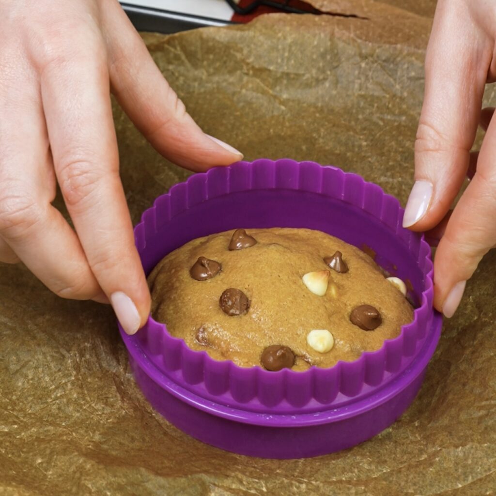 Shaping a freshly baked cookie using a cookie cutter to make it perfectly round.