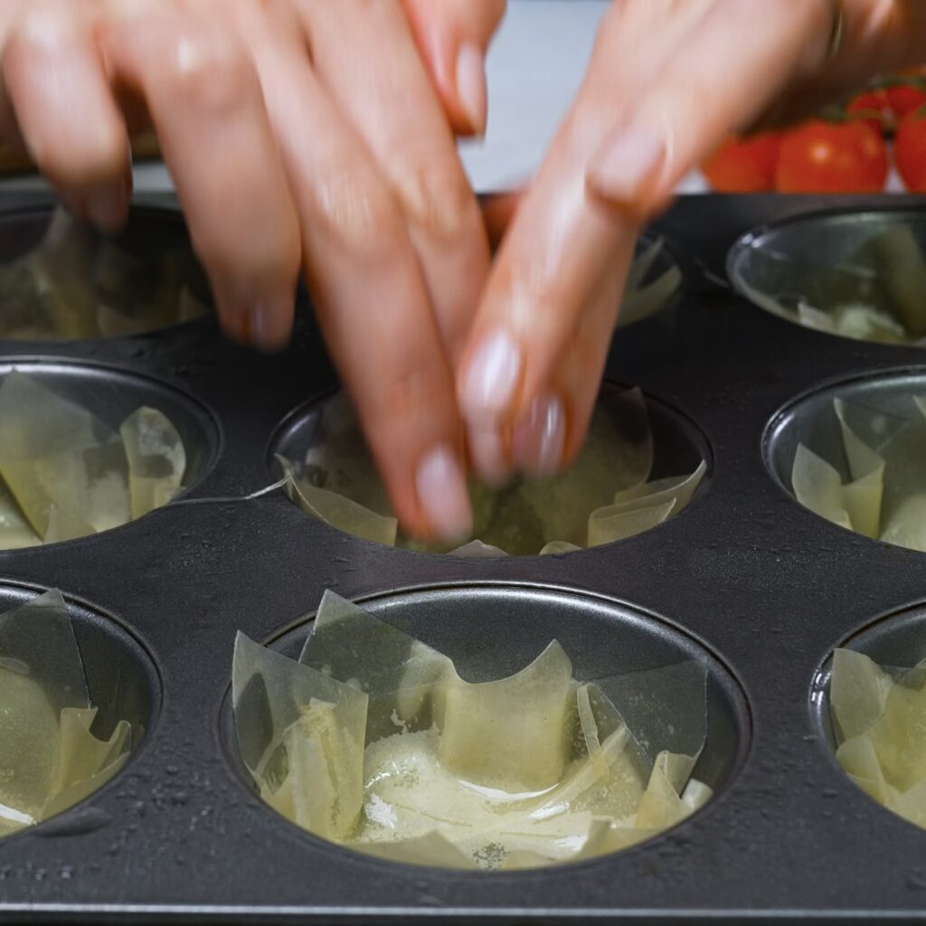 Fitting filo pastry into a muffin tin to form cups.