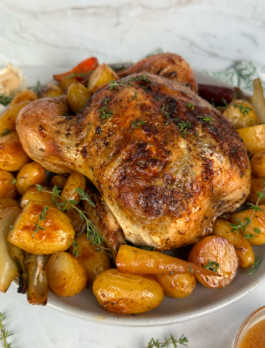 Garlic and herb roasted chicken served with baby potatoes, carrots, fennel, and fresh thyme garnish.