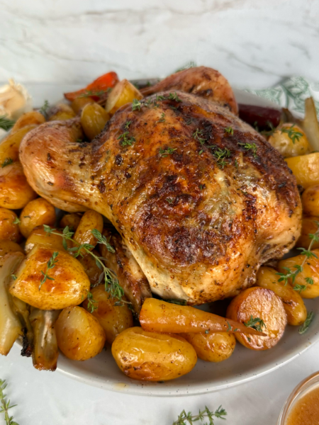 Garlic and herb roasted chicken served with baby potatoes, carrots, fennel, and fresh thyme garnish.