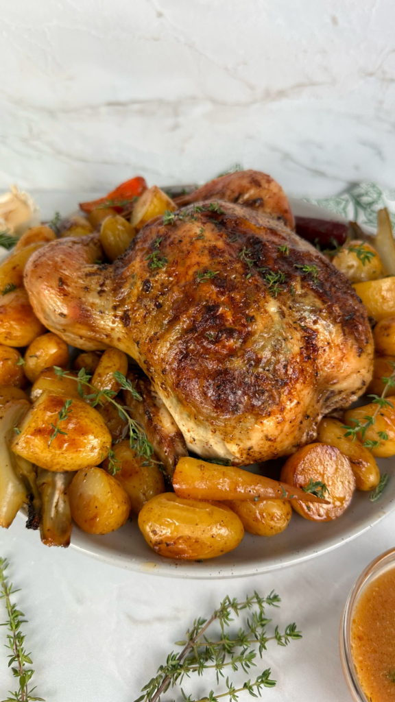 Garlic and herb roasted chicken served with baby potatoes, carrots, fennel, and fresh thyme garnish.