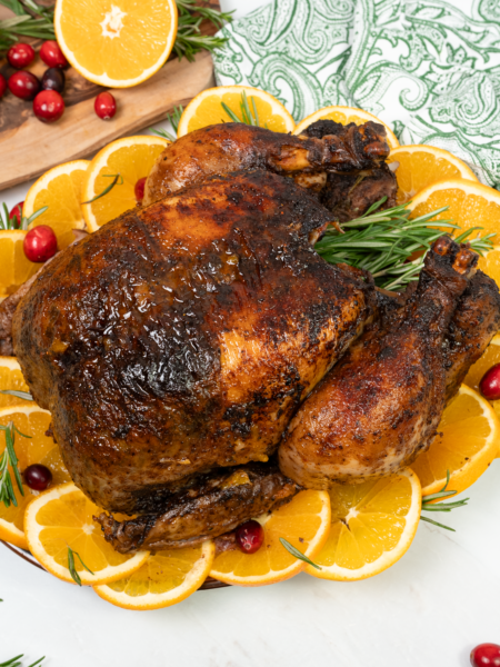 A golden, roasted chicken garnished with cranberries, orange slices, and fresh herbs, ready for the festive table.