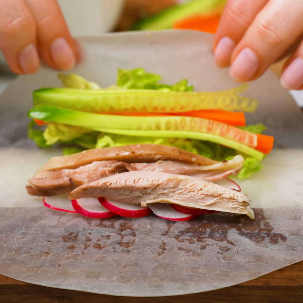 Rolling rice paper with fresh vegetables and shredded chicken.