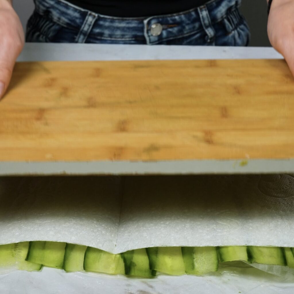 Pressing cucumber slices on rice paper with a cutting board.