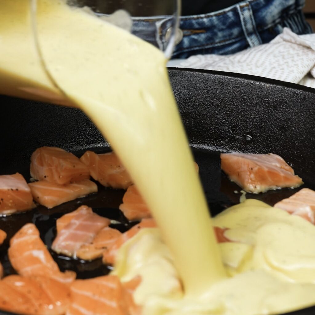 Adding seasoned salmon and batter to the heated skillet for the Salmon Dutch Baby.