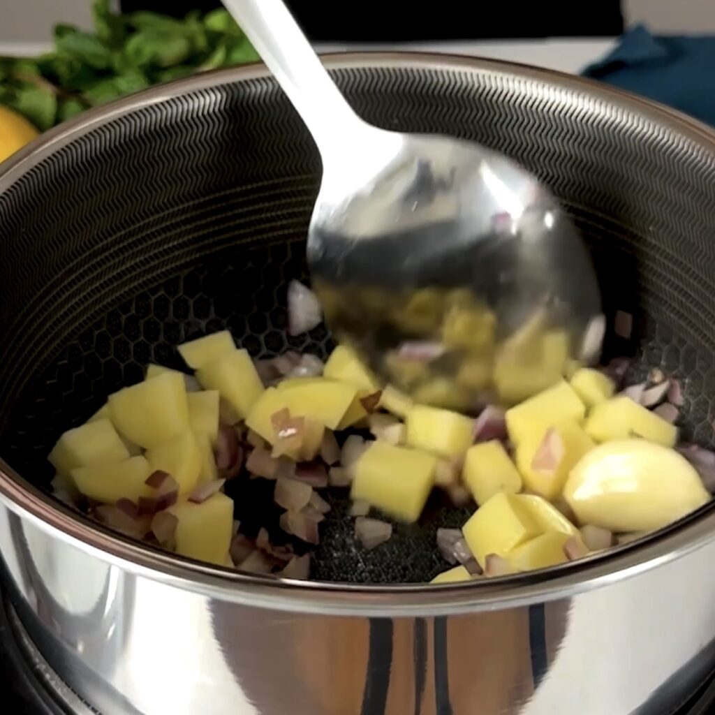 Sautéing diced onion and potatoes in a pot with olive oil.