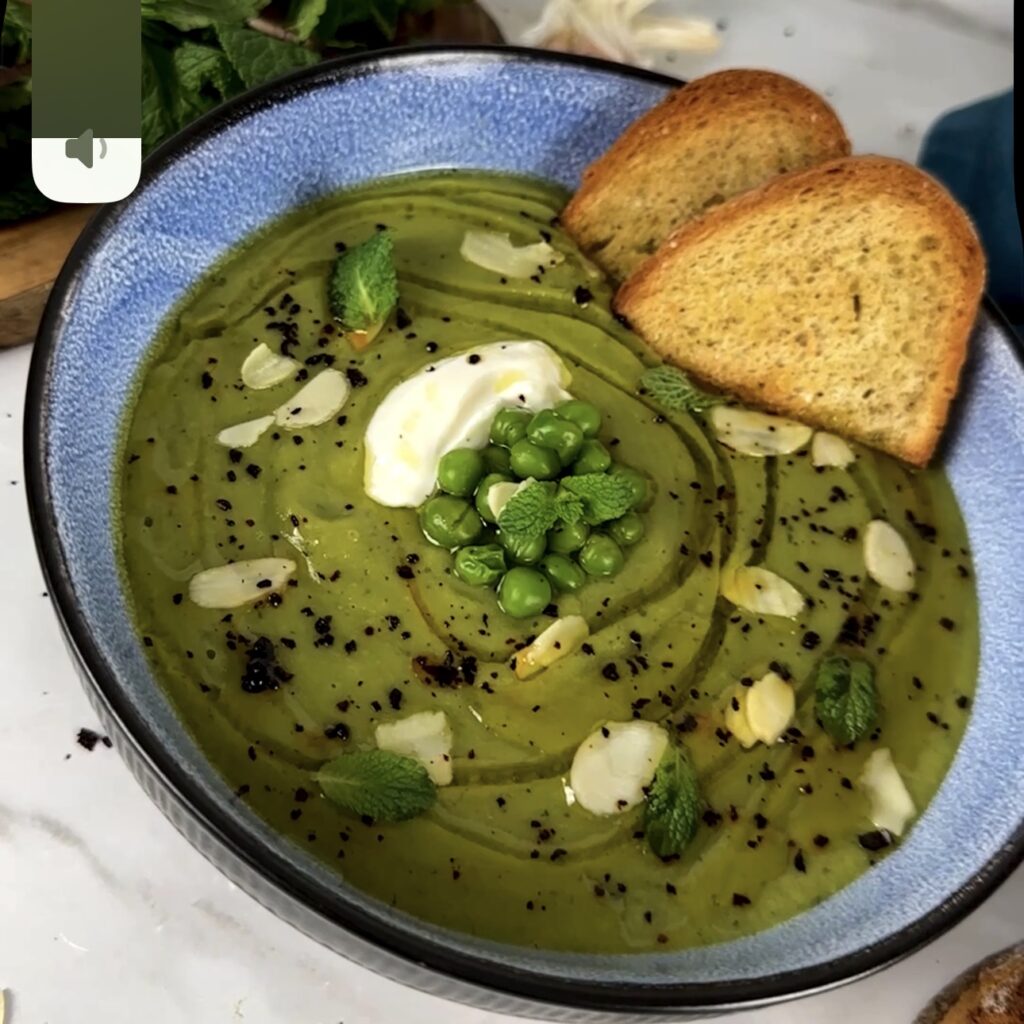 A bowl of creamy pea and mint soup garnished with oat crème fraîche and fresh mint.