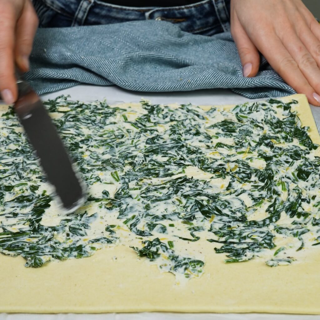 Spreading spinach and ricotta filling evenly over a puff pastry sheet.