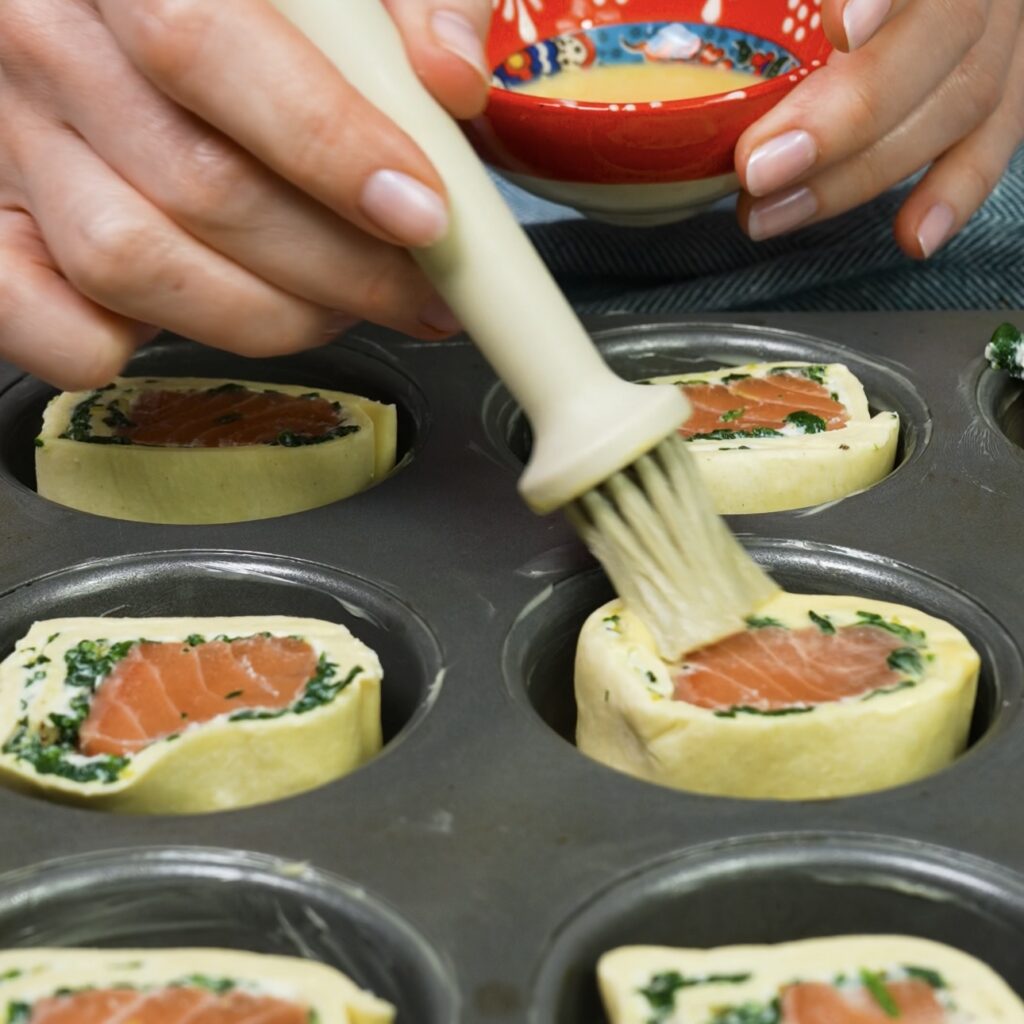 Brushing egg wash over the pastry rolls for a golden finish.