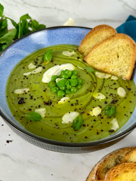 A bowl of creamy pea and mint soup garnished with oat crème fraîche and fresh mint.