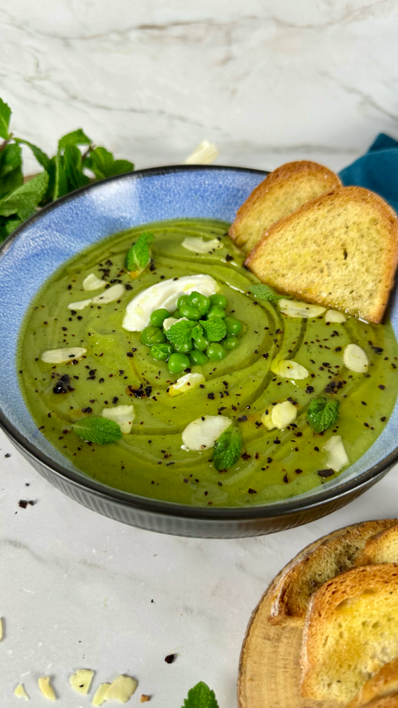 A bowl of creamy pea and mint soup garnished with oat crème fraîche and fresh mint.