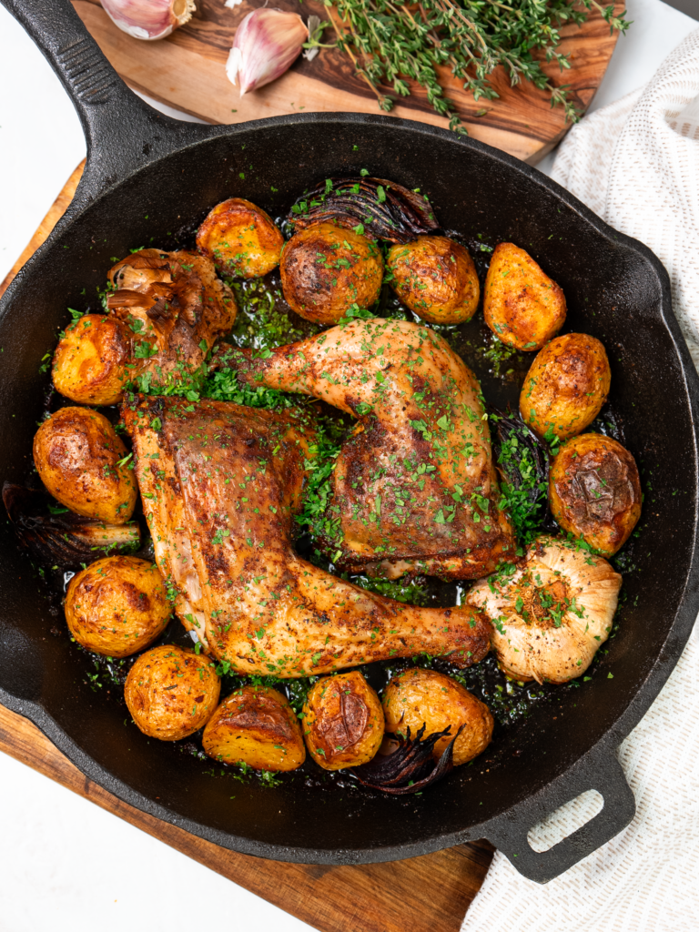 Roasted chicken legs with crispy baby potatoes in a skillet.