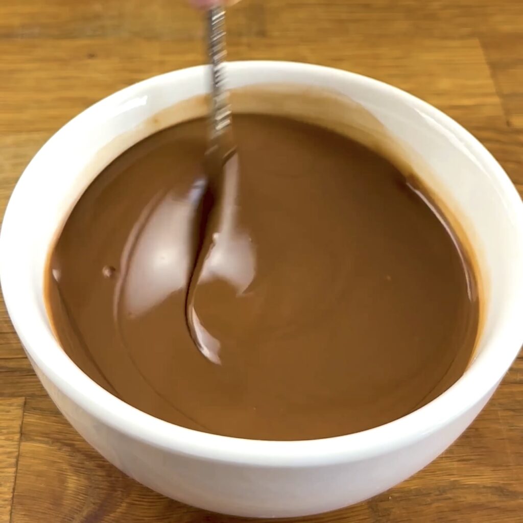 Mixing melted chocolate with sunflower oil in a bowl.