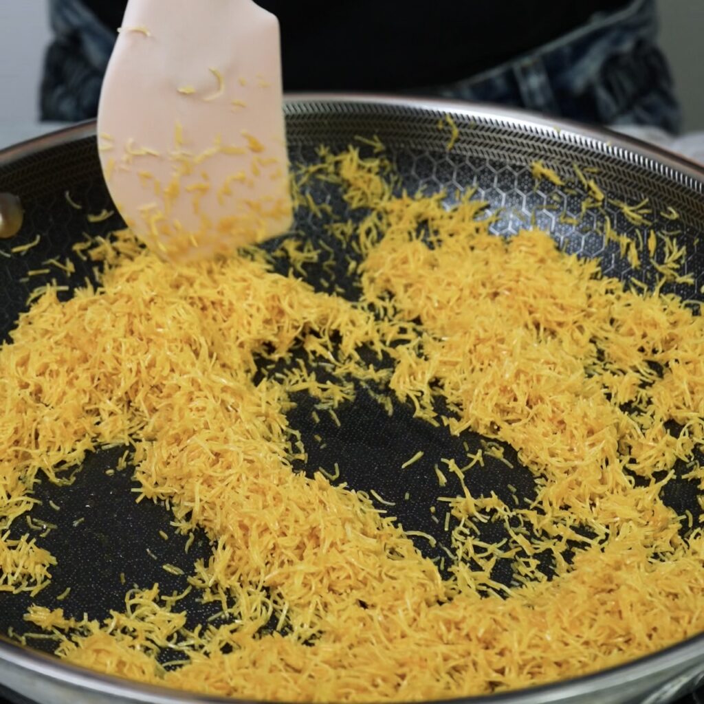 Frying kataifi pastry in a pan until golden and crispy.