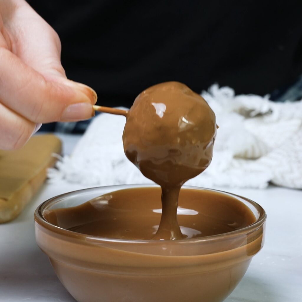 Dipping the rolled date mixture into melted chocolate.