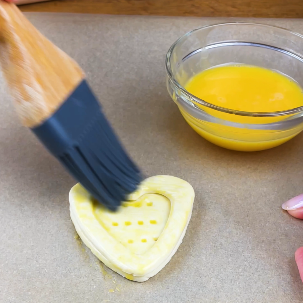 Puff pastry hearts being brushed with egg wash.