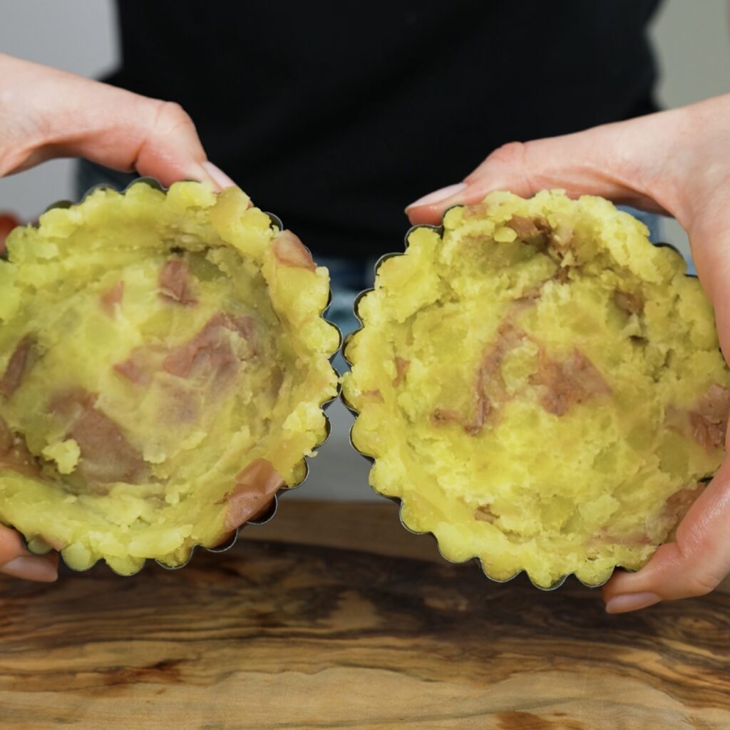 Potatoes pressed into tart tins, forming the base for mini potato tarts.