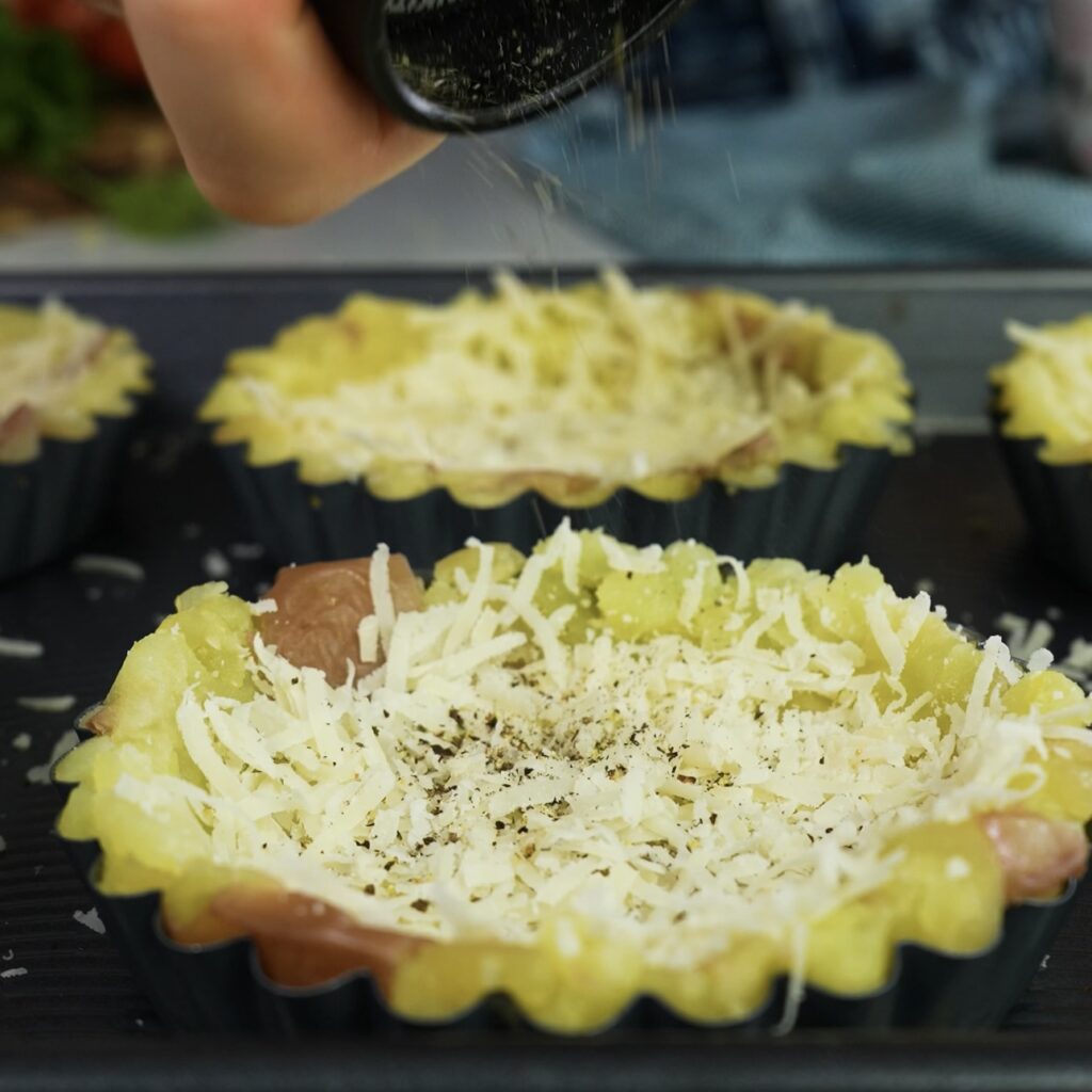 Potato tart shells in tins, sprinkled with Parmesan, salt, and pepper before baking.