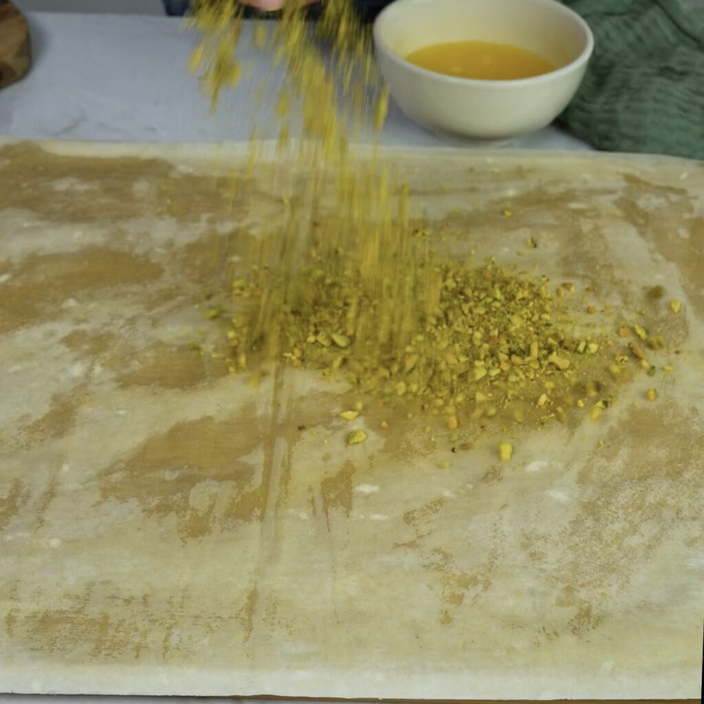 Ground pistachios being sprinkled over a greased filo sheet.