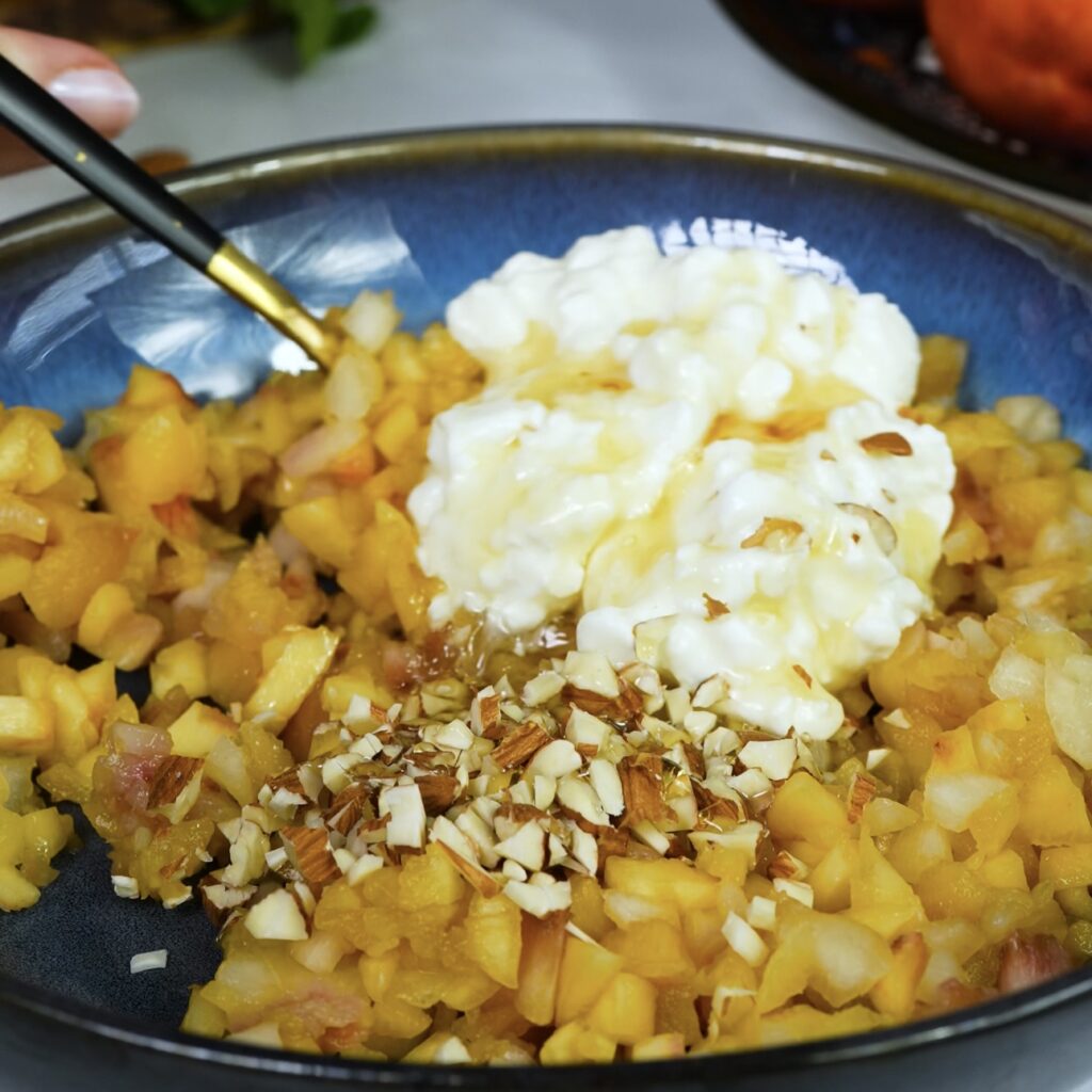 A bowl of cottage cheese, chopped almonds, honey, and nectarine flesh being mixed together.