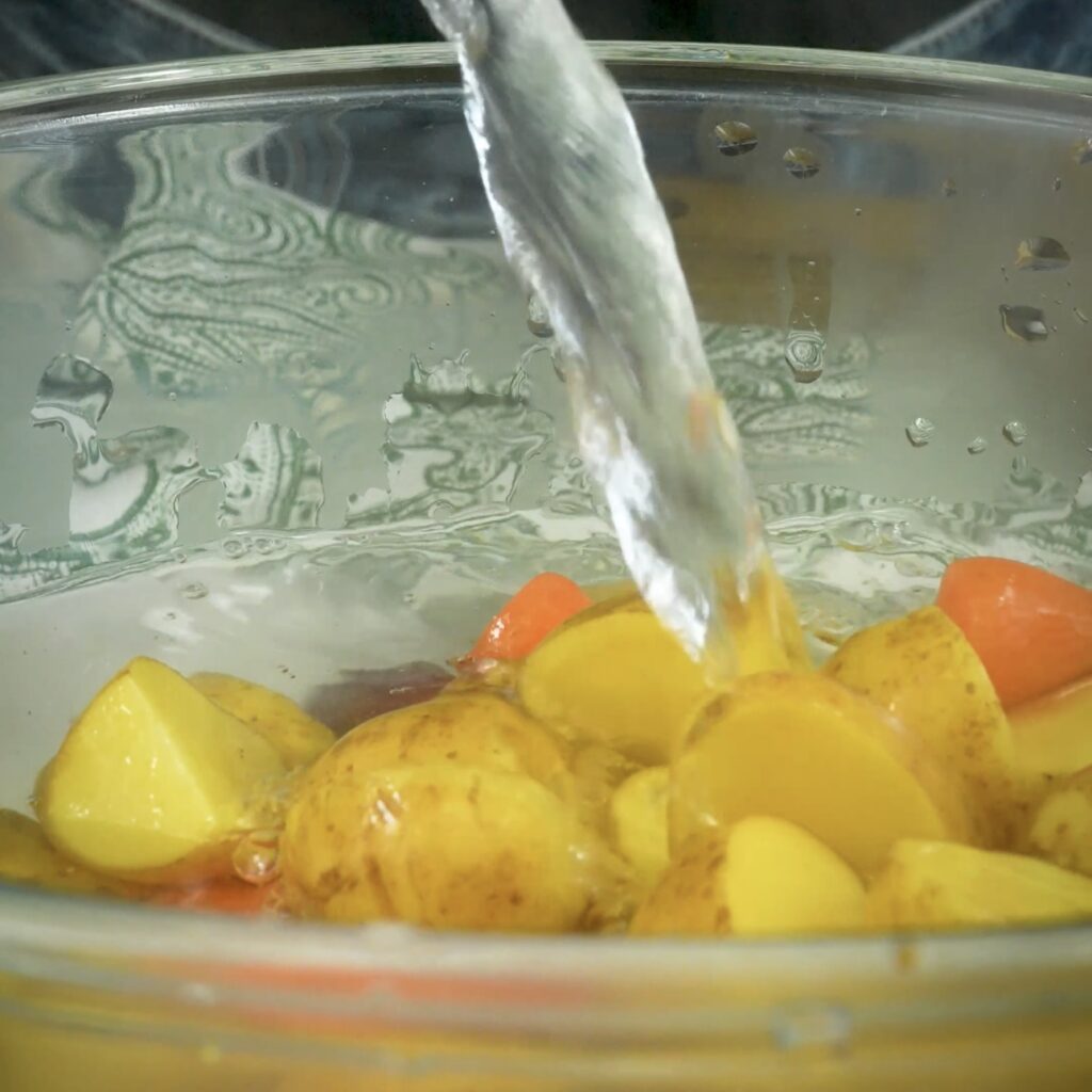 Boiling water being poured over halved baby potatoes and carrots in a bowl