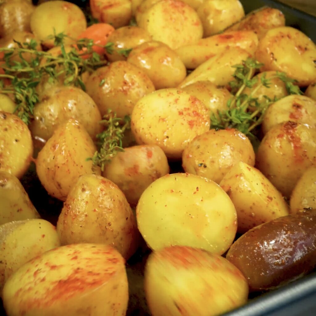 Tossing seasoned baby potatoes and carrots in a baking tray