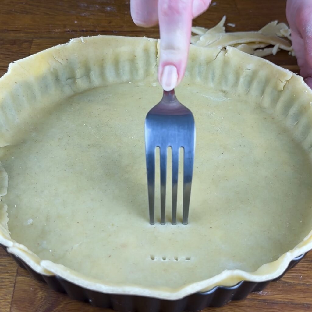 Pricking shortcrust pastry base with a fork in tart tin