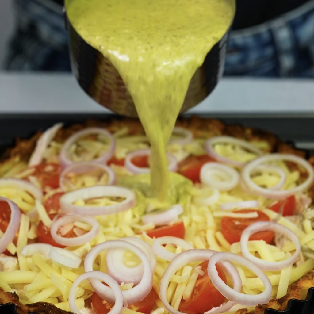 Pouring pesto ricotta custard over quiche filling