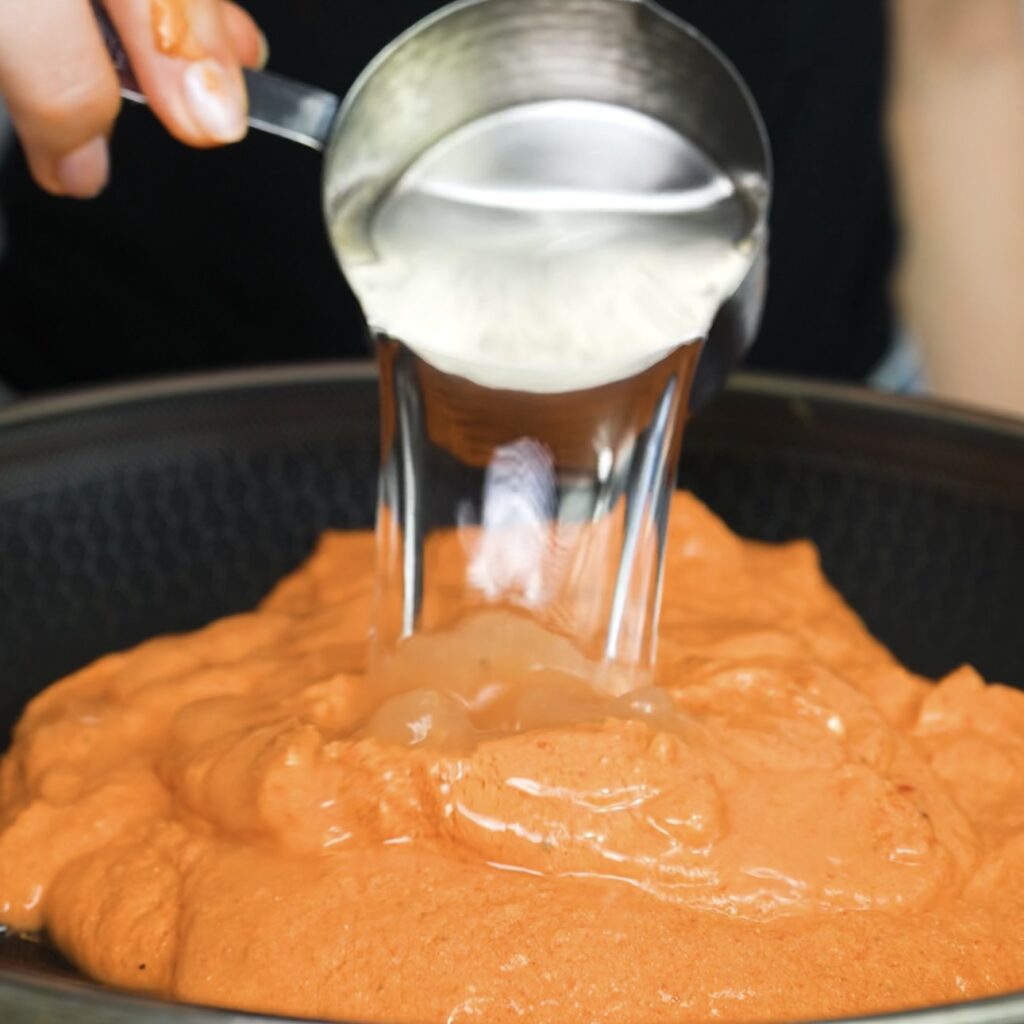 Adding pasta water to loosen the sauce.