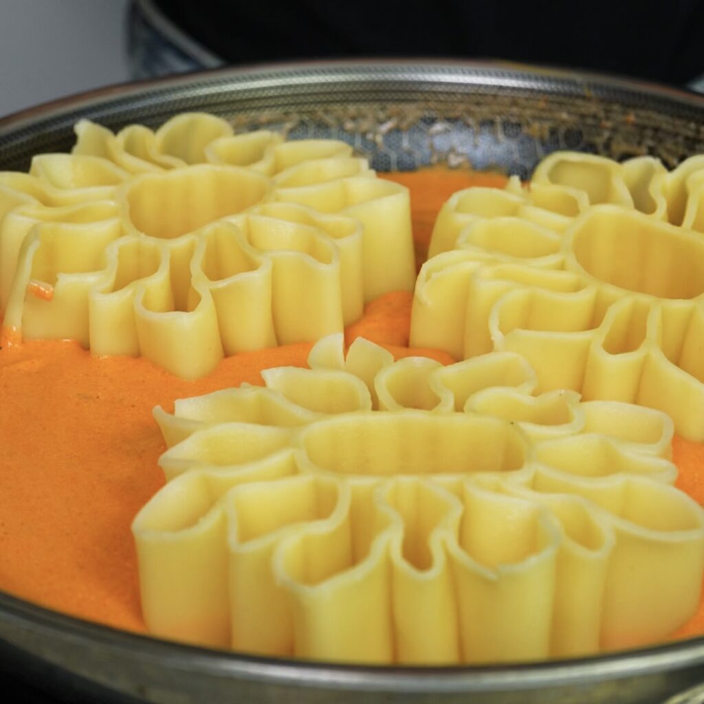 Mixing cooked pasta with roasted pepper sauce.