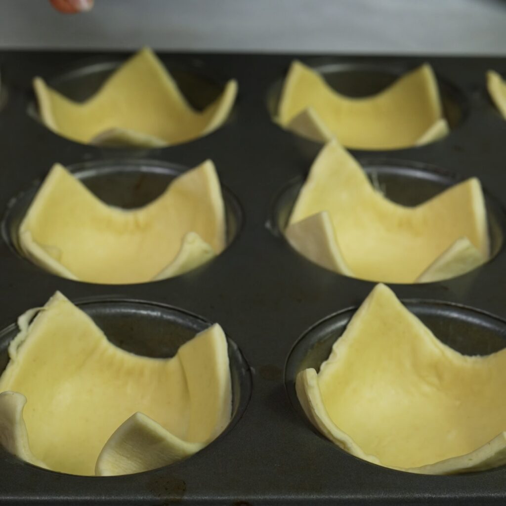 Muffin tin lined with puff pastry squares, ready for filling