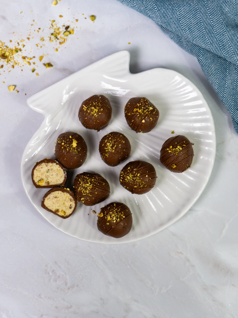Finished cottage cheese date bite coated in chocolate and topped with crushed pistachios