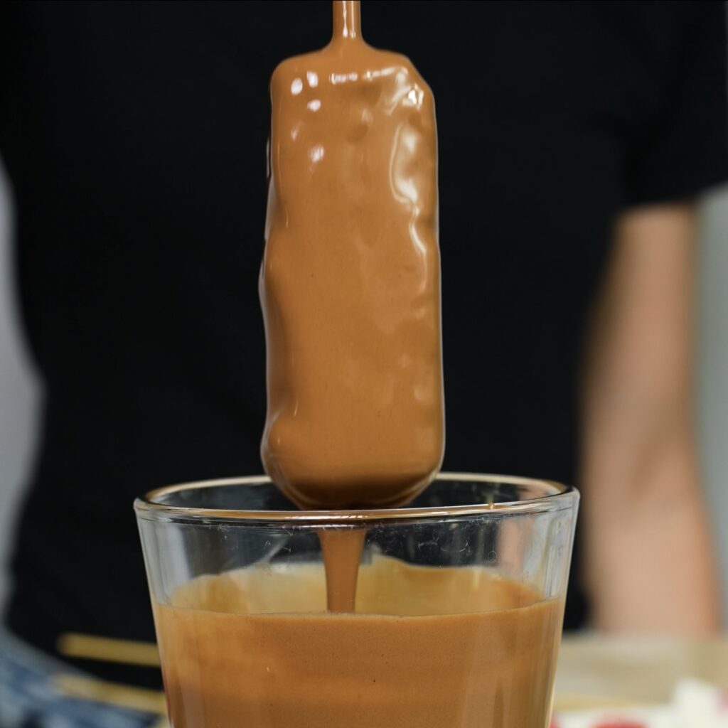 Dipping a frozen raspberry cottage cheese bar into melted chocolate